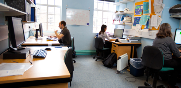 Room with 4 computers desks and 3 people using 3 of them